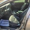 The image shows the interior of a silver 2013 Kia Optima EX with the driver’s door open, featuring black seats, a dashboard, and a floor mat that says “YOUR BUSINESS IS APPRECIATED!” with outlined footprints.