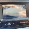 The 2013 Kia Optima EX’s rearview camera displays red, yellow, and green parking guidelines with a “Warning! Check your surroundings for safety” alert; dashboard buttons are positioned just beneath the screen.