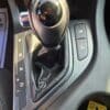 Close-up of the 2013 Kia Optima EX gear shift lever in automatic mode, showing park, reverse, neutral, drive, manual (+/-), and heated seat buttons with driver and passenger seat icons.