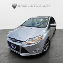 A 2014 Ford Focus SE sedan in silver is shown in a showroom, angled left to highlight the front and driver’s side, with the BOSS AUTO SALES logo visible on the wall behind it.