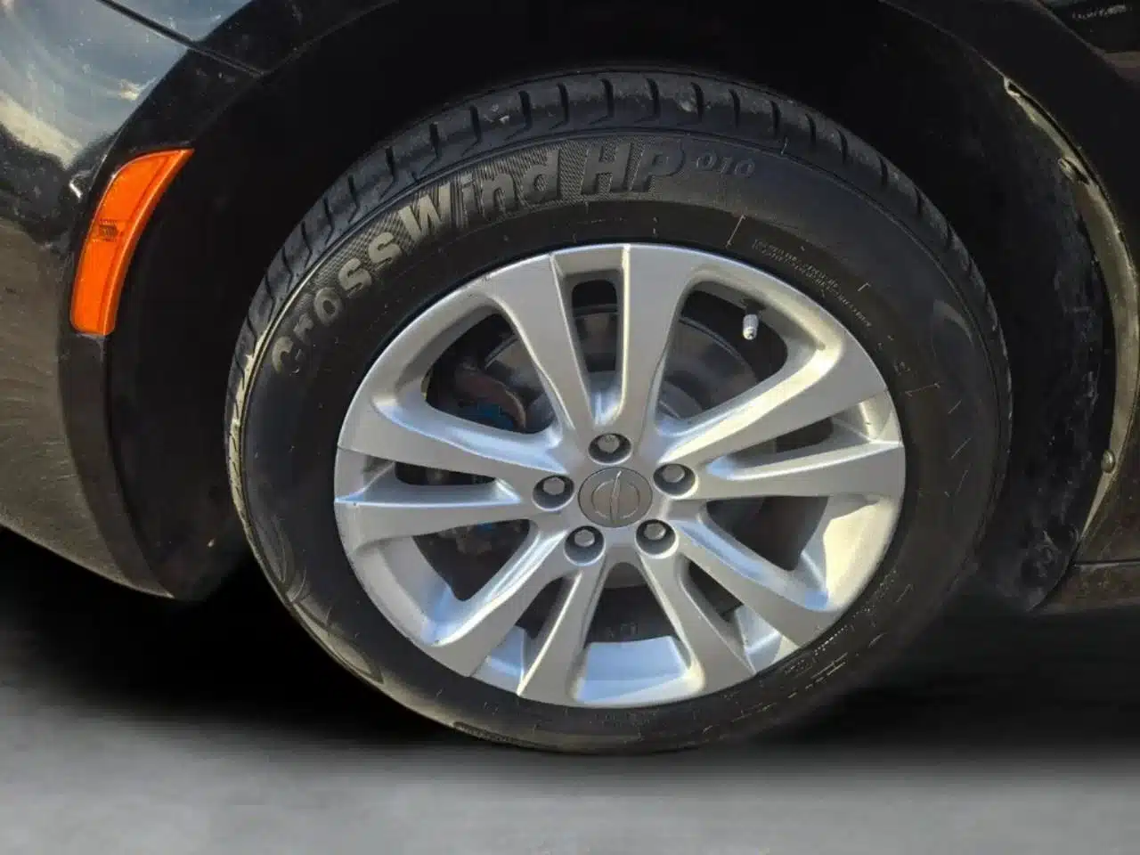 Close-up of a black CrossWind HP010 tire mounted on a silver alloy rim, featured on a 2015 Chrysler 200 Limited—captured on a concrete surface, ideal for viewers seeking detailed visuals of this high-quality used car.
