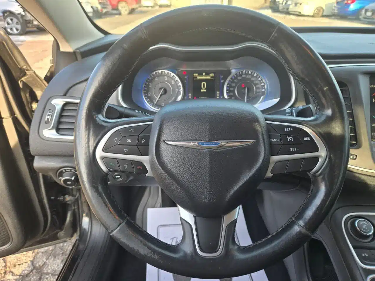 Interior view of the 2015 Chrysler 200 Limited from the driver’s seat, featuring the steering wheel with integrated control buttons and a dashboard displaying illuminated gauges and a digital speedometer.
