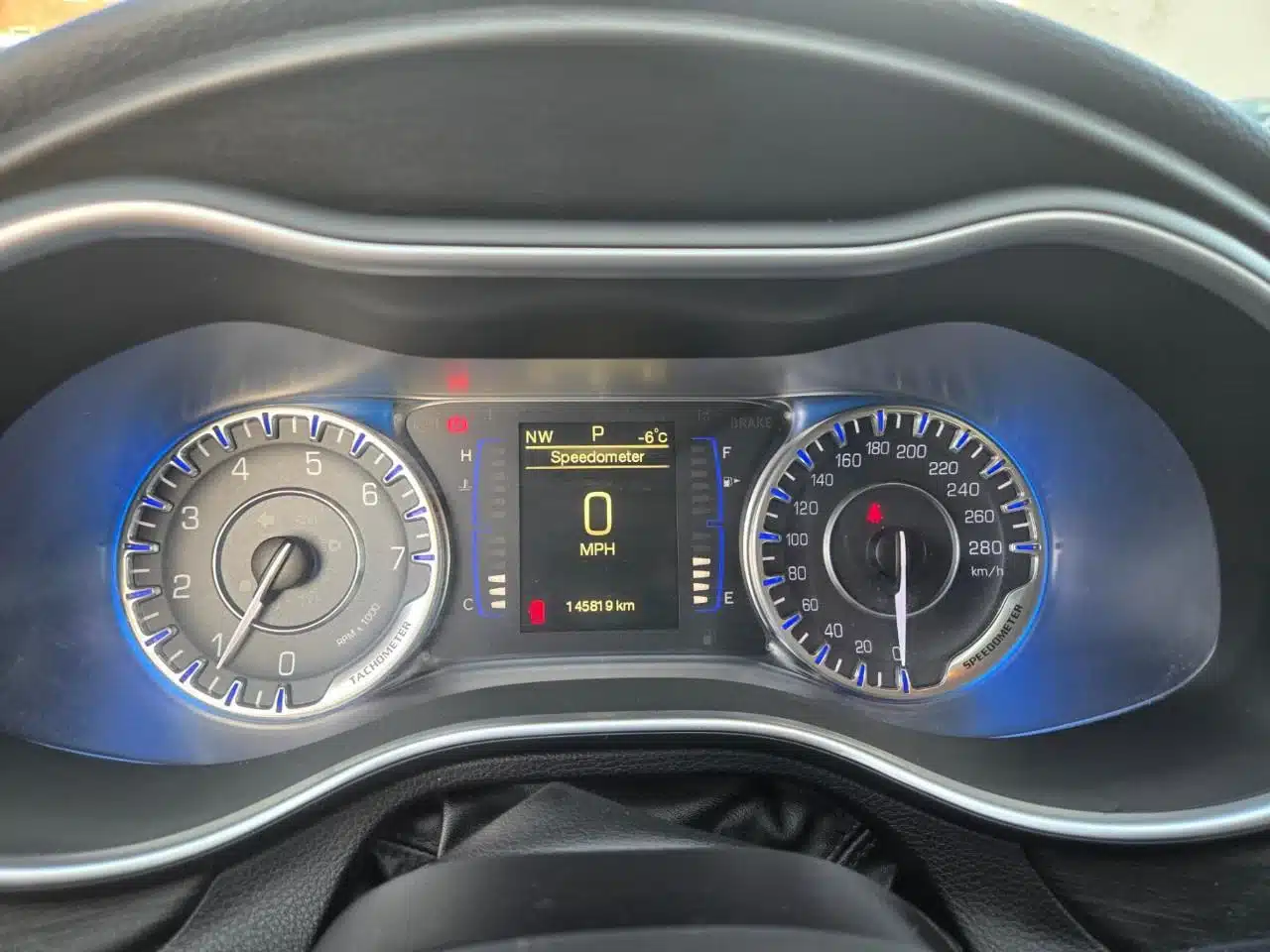 The dashboard of the 2015 Chrysler 200 Limited features a digital display with the speedometer reading 0 MPH, an odometer at 145,910 km, a temperature of -8°C, and a fuel gauge. Blue-accented analog speedometer and tachometer are also present.