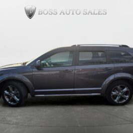 A 2015 Dodge Journey Crossroad in dark gray is shown from the side in a showroom, with Boss Auto Sales signage above it. The SUV features alloy wheels and roof rails. A 2015 Dodge Journey Crossroad in dark gray is shown from the side in a showroom, with Boss Auto Sales signage above it. The SUV features alloy wheels and roof rails.