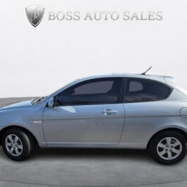 A 2009 Hyundai Accent GL Hatchback in silver is shown in profile on a gray concrete surface, with the Boss Auto Sales logo and text visible in the background.