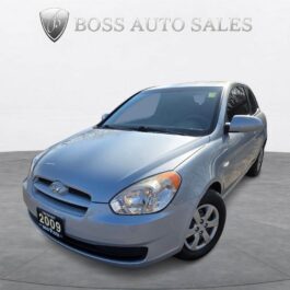 A 2009 Hyundai Accent GL Hatchback in silver is displayed in a showroom with BOSS AUTO SALES on the wall behind, angled to showcase its sleek front and driver’s side.