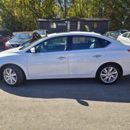 A white sedan parked on an asphalt lot in front of a small office building.